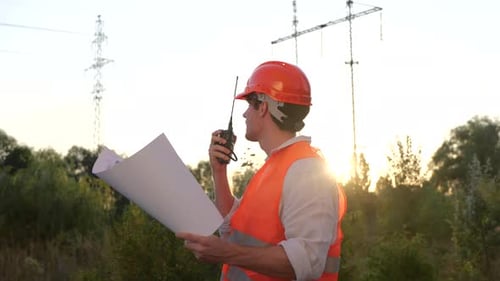 Electrical Engineer Talking on the Walkietalkie and Holding Drawing While Controlling of Repair of