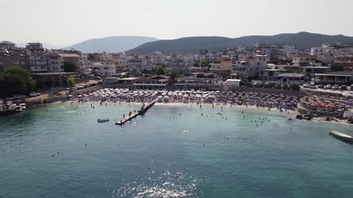 Beach packed with tourists in popular coastal town Ksamil, Albania; aerial