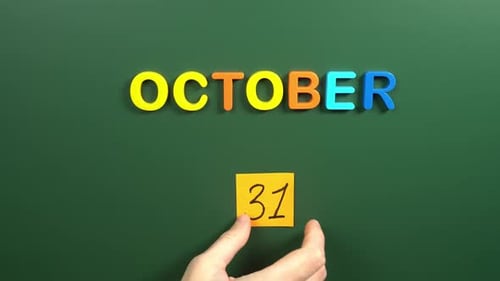 Hand sticking a sticker 31 October calendar day on school board. 31 date of October. Thirty first