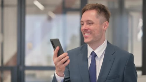 Smiling Businessman Using Smartphone in Modern Office