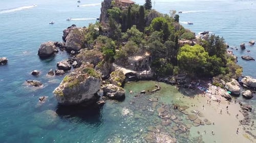 Drone shot of Isola Bella in Taormina, with people relaxing on the beach shore.