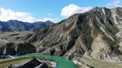 Aerial View of a Turquoise River and Road Snaking Through a Mountainous Terrain
