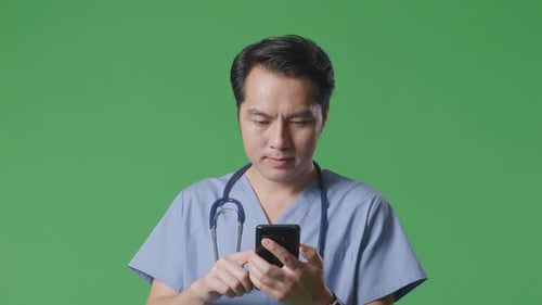 Close Up Of Asian Male Doctor With Stethoscope Using Smartphone While Walking On Green Screen