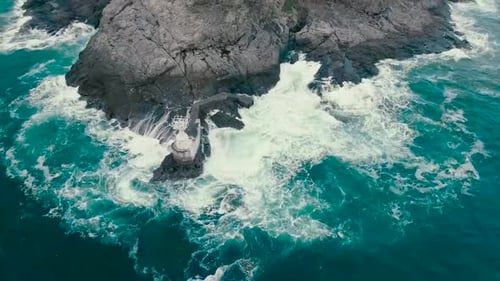 Spinning aerial drone video of blue and green ocean sea water hitting the shoreline where steep clif