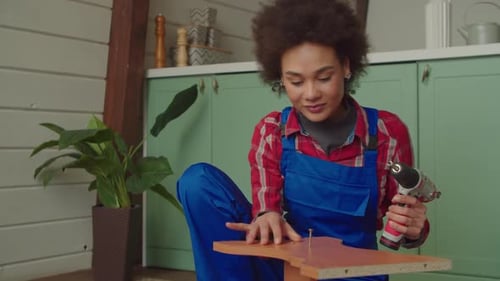 Pretty African American Woman Assembling DIY Furniture with Cordless Screwdriver