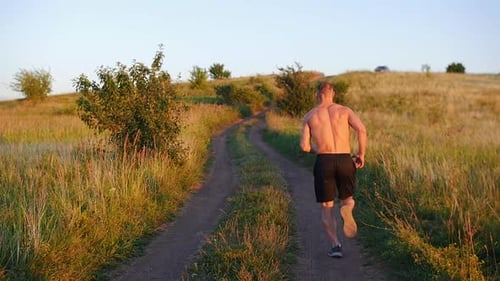 Muscular Shirtless Man Jogging Up the Hill at Sunset in Slow Motion