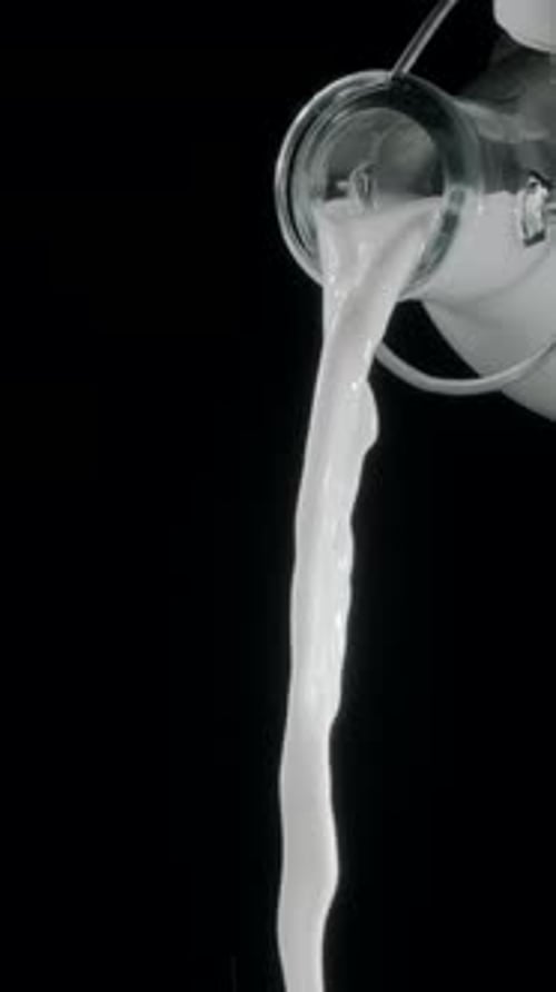 Pouring milk from a bottle of milk into the glass on black background.
