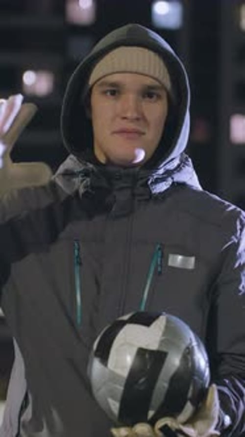 Man in Hoodie Hitting Soccer Ball on Urban Sports Field at Night