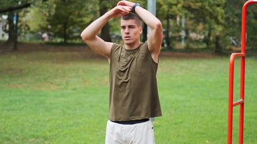 Athletic young man stretches muscles before starting training in park