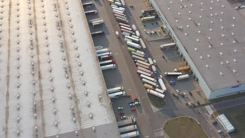 Semi truck with cargo trailer is travelling along a parking lot of a warehouse in the logistics park