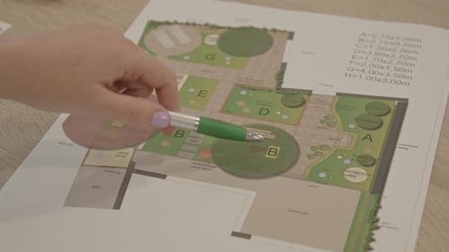 A garden plan with several details being pointed out by a pen held by a female hand - close up