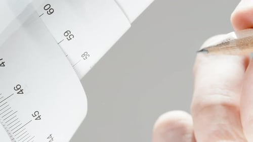 The male hand takes measurements on the glass using a pencil and a paper ruler.
