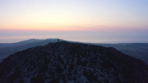 Aerial - Flying from front to behind the man standing on top of the mountain watching beautiful suns