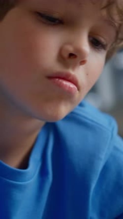 Closeup of a Focused Young Child in a Blue Shirt Drawing and Writing on Paper with a Yellow Marker