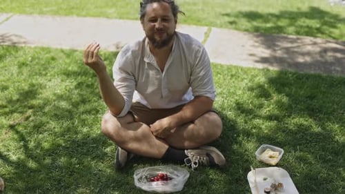 Man with Dreadlocks Eating Cherries During a Park Picnic