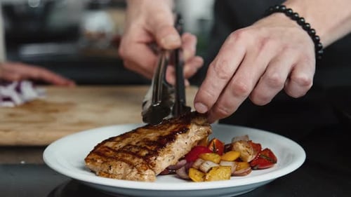 Hand of Chef Putting Grilled Steak on Plate