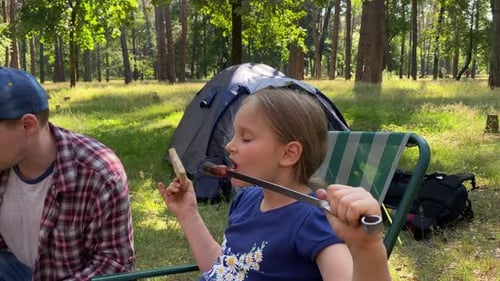 Child Enjoys Camping Hotdog with Adult in Forest