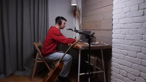 Young Male Musician Creating Audio Content in a Home Studio Wearing Headphones and Using a Laptop
