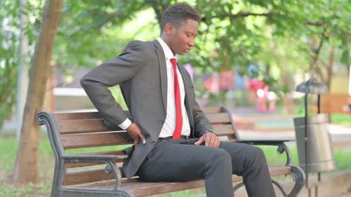 Young Businessman with Back Pain on Park Bench