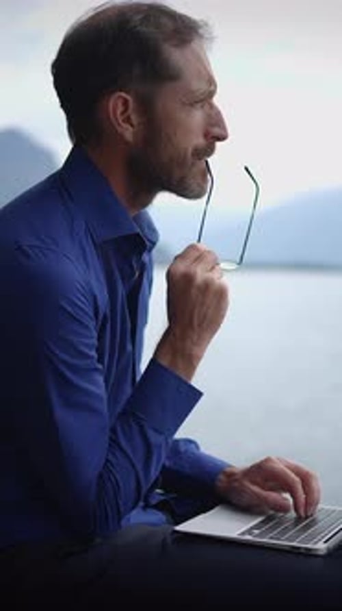 A Professional Man is Diligently Working By the Serene Lake While Using His Laptop Computer