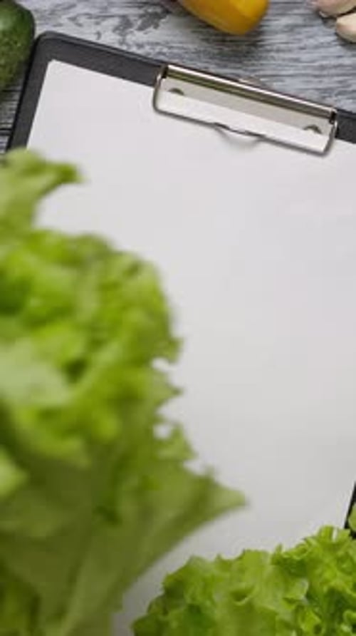 Vertical of Cook Taking Lettuce From Table with Blank Paper Clipboard