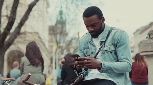Close Up Young African American Man Uses the Phone Sitting Outdoor at the Street Business Shopping