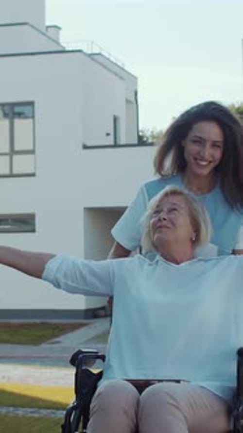 Young Woman Pushing Senior in Wheelchair Outdoors