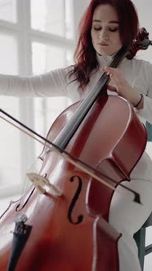Beautiful Woman Sitting and Playing the Cello in a Studio on a White Background