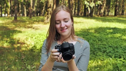 A Young Girl Photographer with a Camera Poses in the Park