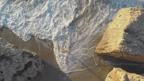 Drone aerial view of young woman walking on the beach towards the sea from top down in Nerja