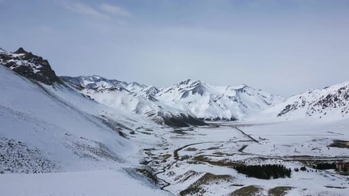 Aerial view drone flying over beautiful white snowy mountains landscape and a cloudy sky.