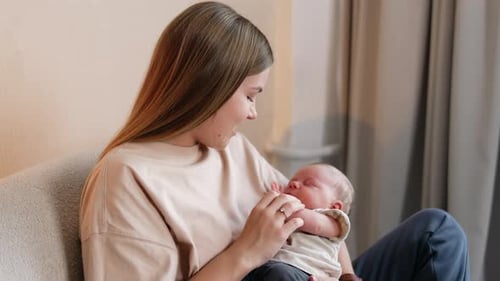Woman with long blonde hair holding her baby. Mother takes tiny hand of a child and smiles to a kid.