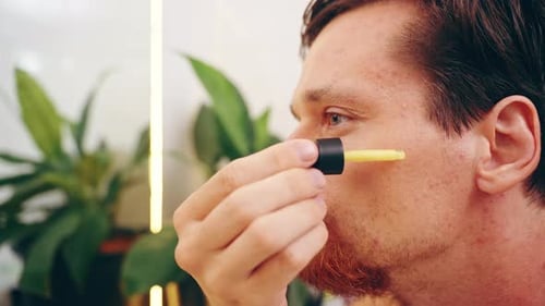 Man Applying Yellow Retinol Serum with Dropper onto Cheek While Looking in Mirror, Close-Up Side Vie