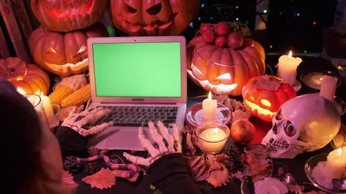 Creepy skeleton typing invitation on laptop with green chromakey screen inviting friends to party