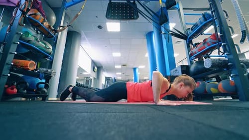 Young sportswoman doing push-ups on a mat. Side view of a girl training on the floor in the gym.