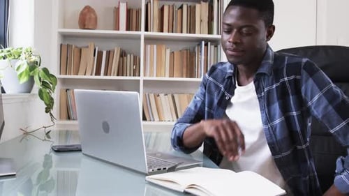 African American man working on laptop and writing notes at home office