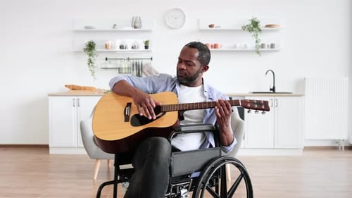 Man in Wheelchair Plays Guitar Indoors