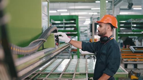 Green colored machine, operator is busy. Factory worker is indoors with hard hat.
