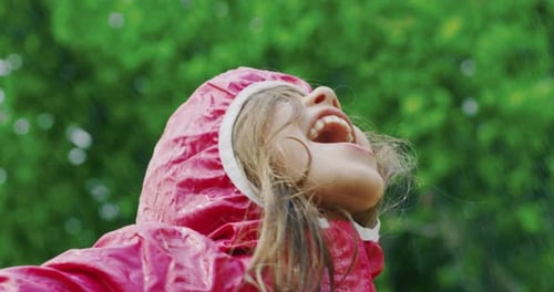 Authentic shot of cute happy little girl in raincoat is having fun and enjoying the rain in a hot