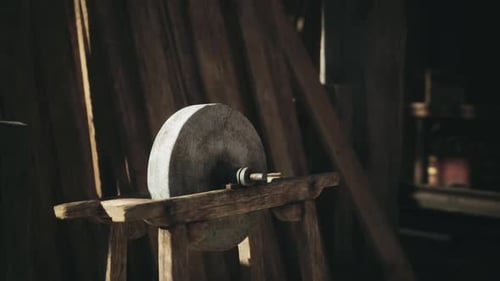 A Weathered Grinding Stone Rests on a Wooden Stand Inside a Dimly Lit Workshop