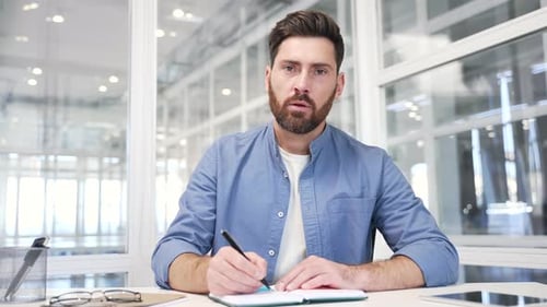 Webcam view. Businessman watching video call conference takes notes in notebook looking at camera