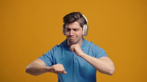 Young Positive Man Listening Music Enjoying With Headphones on Yellow Studio