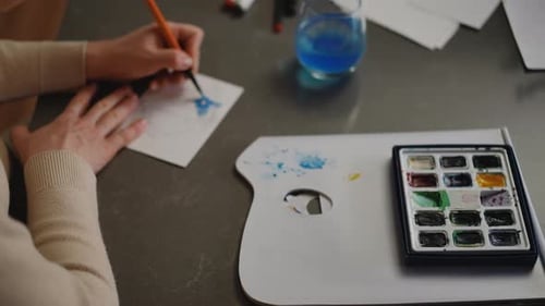 Nahaufnahme Aquarellfarben auf einer weiß figurierten Farbpalette liegen auf dem Tisch Eine Frau malt eine