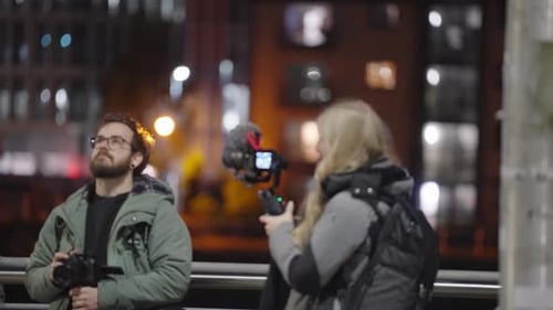 Man and Woman Hold Cameras at Night