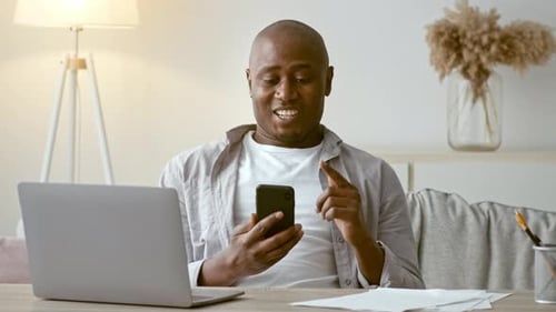 Man Smiling While Using Phone at Desk
