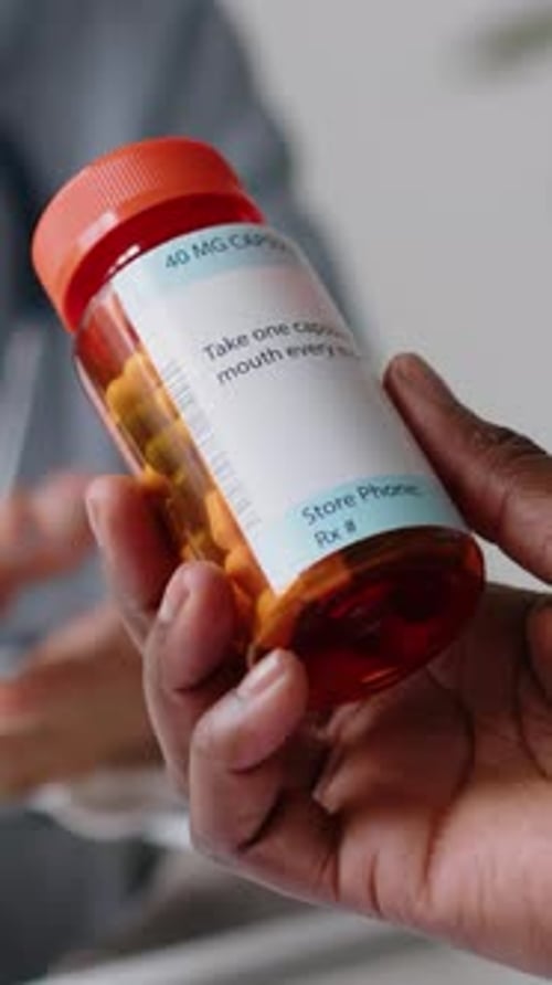 Hand of Anonymous Patient Holding Jar of Prescription Pills in Clinic