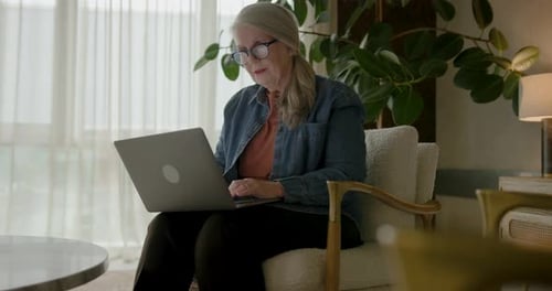 Senior Woman Using Laptop at Home in Armchair