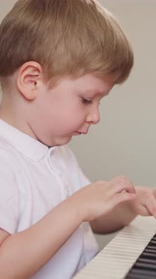 Little Boy Puts Elbows on Piano Keyboard and Leans on Hands