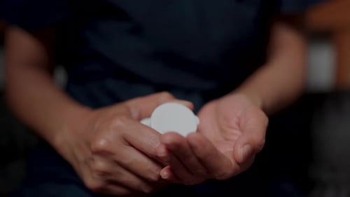 Frau zeigt, wie man Medikamente auf ihre Hand gießt. Sie liegt mit einer chronischen Krankheit im Bett.