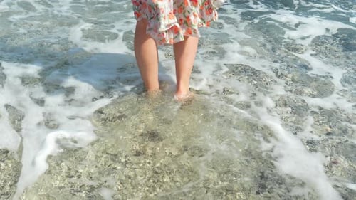 Woman in summer dress walking into Atlantic ocean barefoot, back view